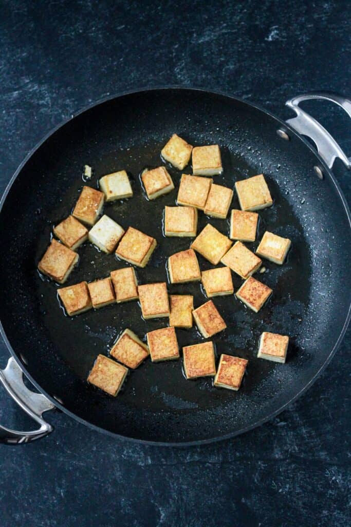 Cubes of tofu frying in a skillet.