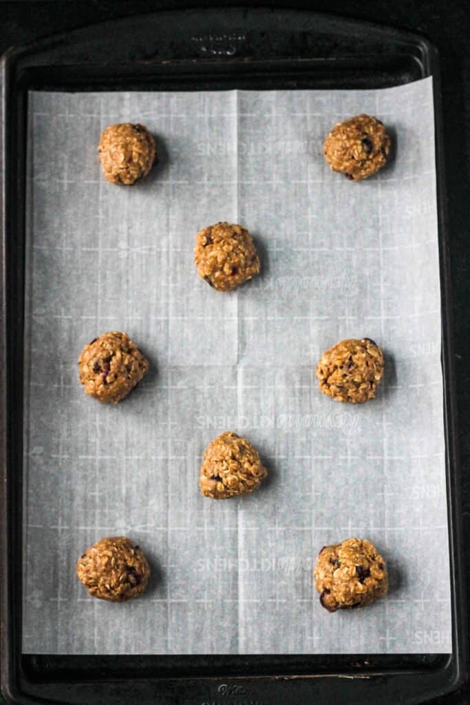 Eight raw cookie dough balls on a cooking sheet.
