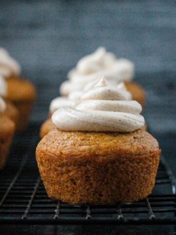 Close up of one frosted vegan pumpkin cupcake on a cooling rack.