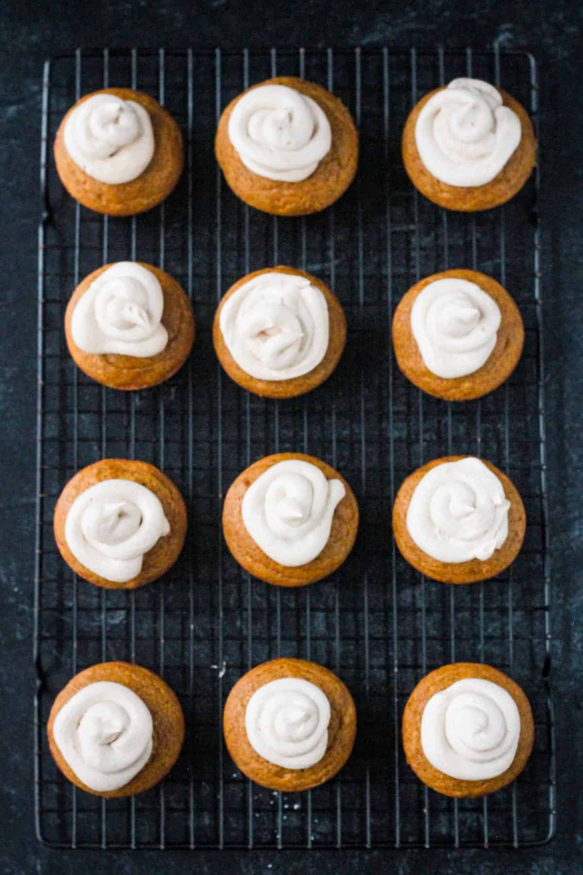 Twelve frosted vegan pumpkin cupcakes on a wire cooling rack.