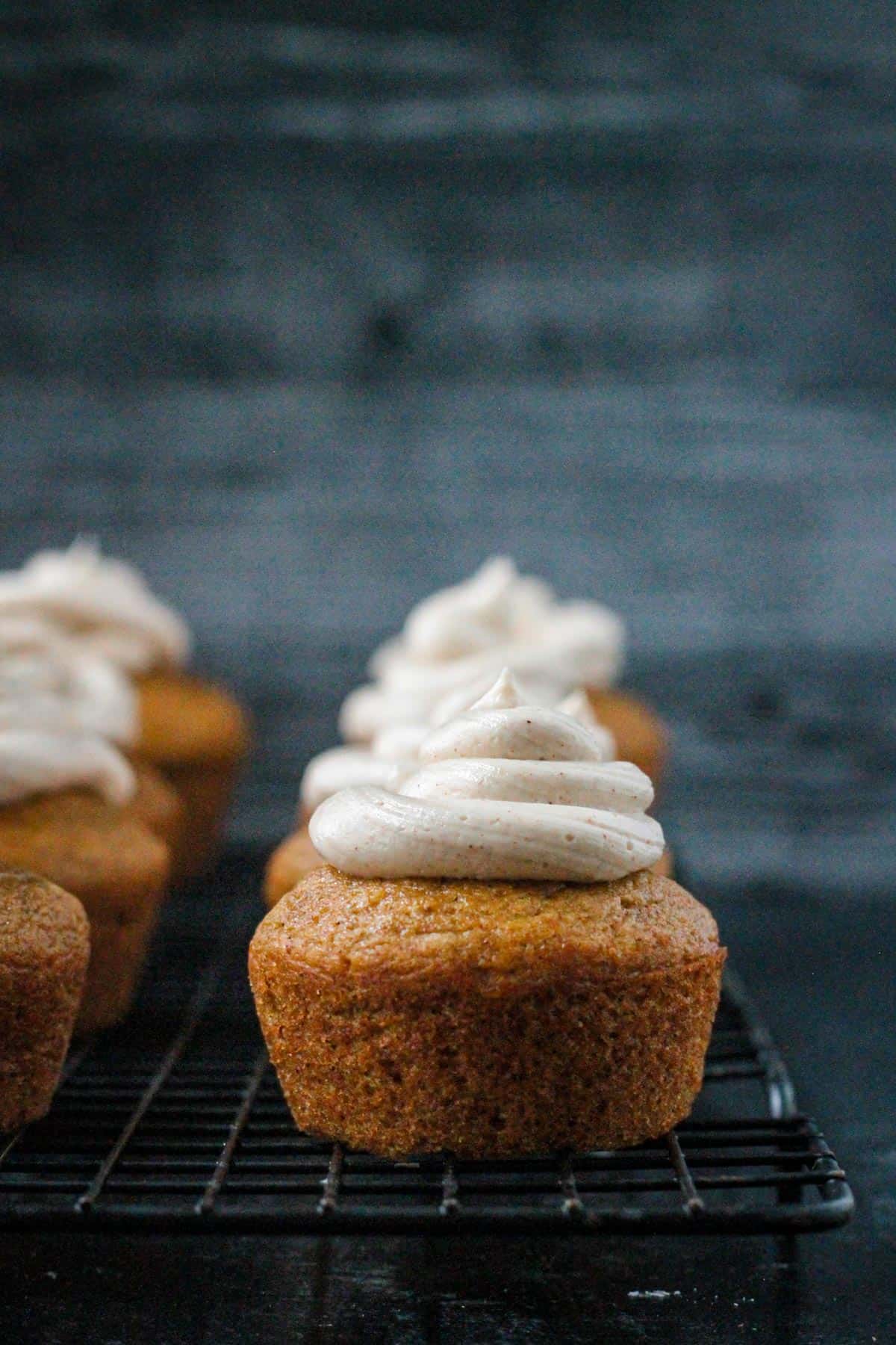 Close up of one frosted vegan pumpkin cupcake on a cooling rack.