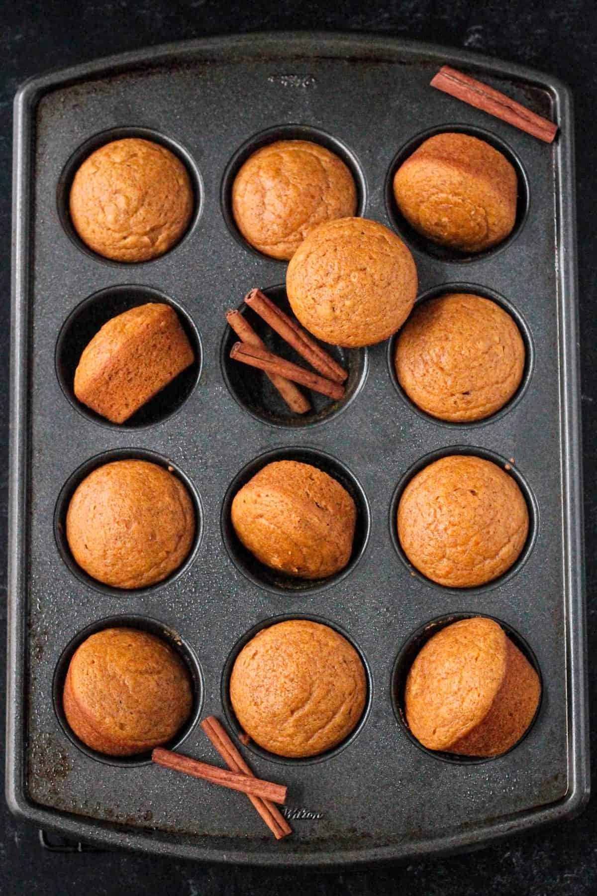 Baked vegan pumpkin cupcakes arranged haphazardly in a cupcake pan.