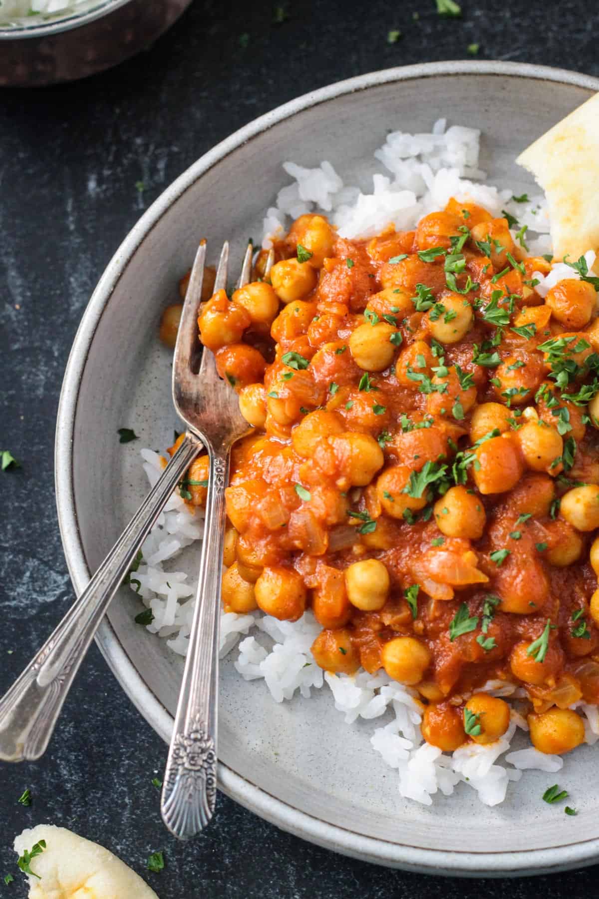 Two forks on a plate of vegan tikka masala with chickpeas and rice.
