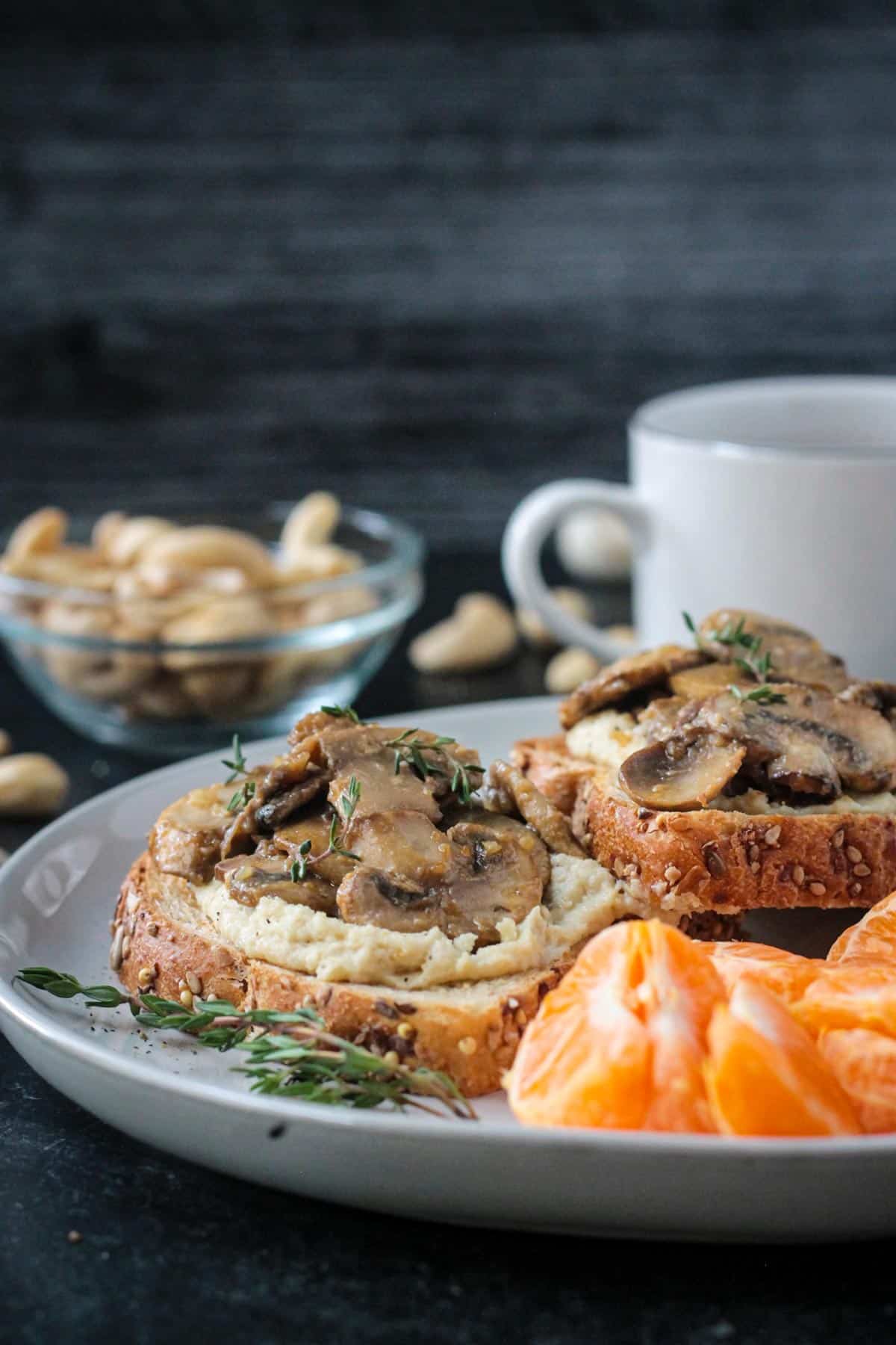 Plate of creamy vegan mushroom toast next to oranges and a cup of coffee.