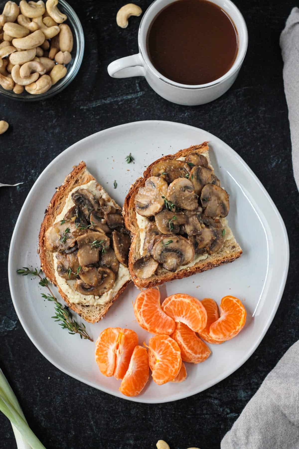 Two slices of creamy mushroom toast on a plate with a pile of orange segments.