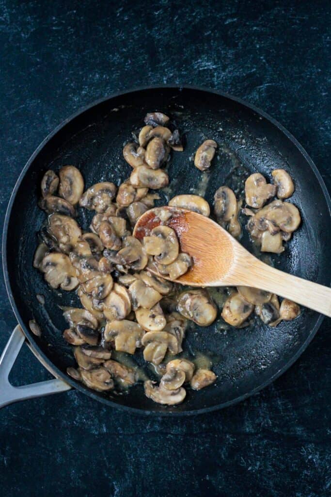 Sautéed creamy miso mushrooms in a skillet with a wooden spoon.