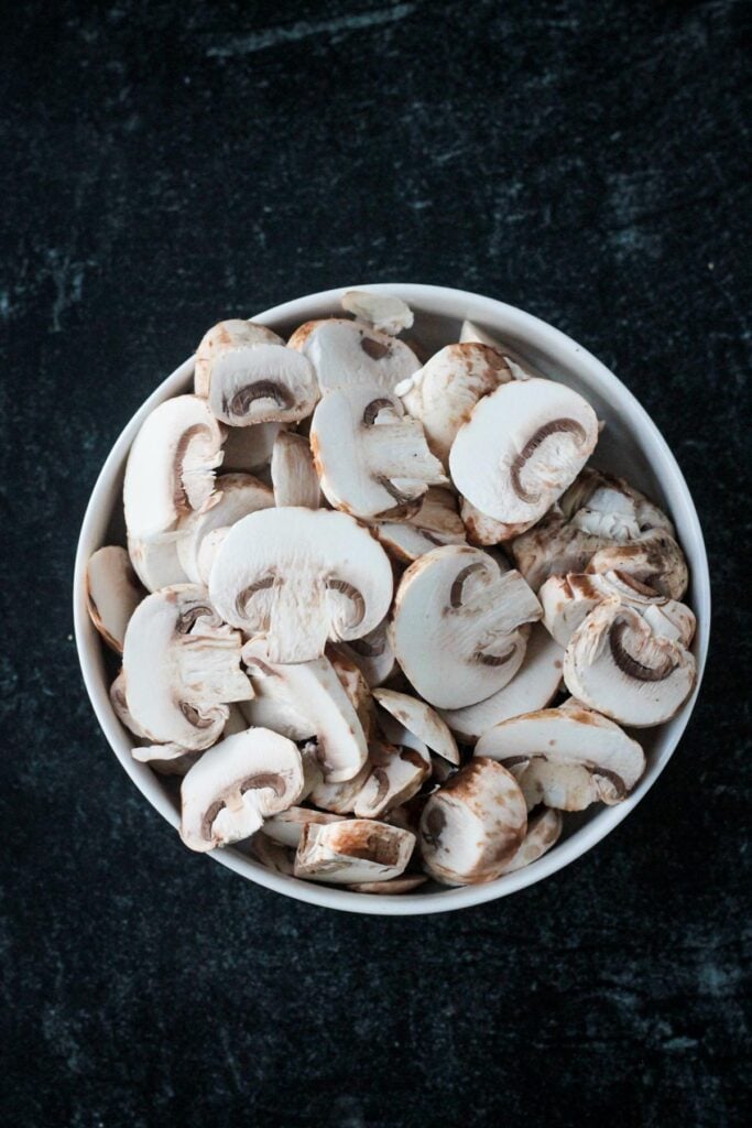 Sliced button mushrooms in a bowl.