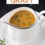 Small white pitcher of gravy garnished with fresh thyme leaves.