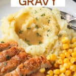 Close up of mashed potatoes topped with gravy on a plate with vegan chicken and corn.