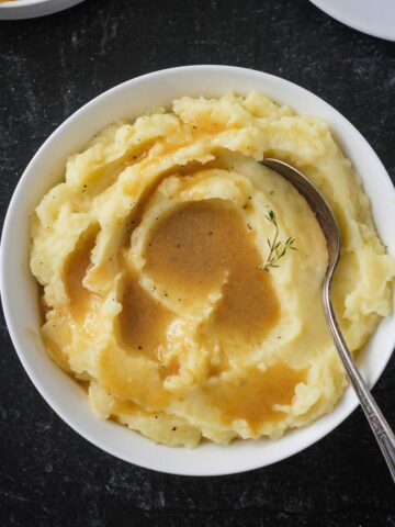 Bowl of mashed potatoes topped with vegan gravy.