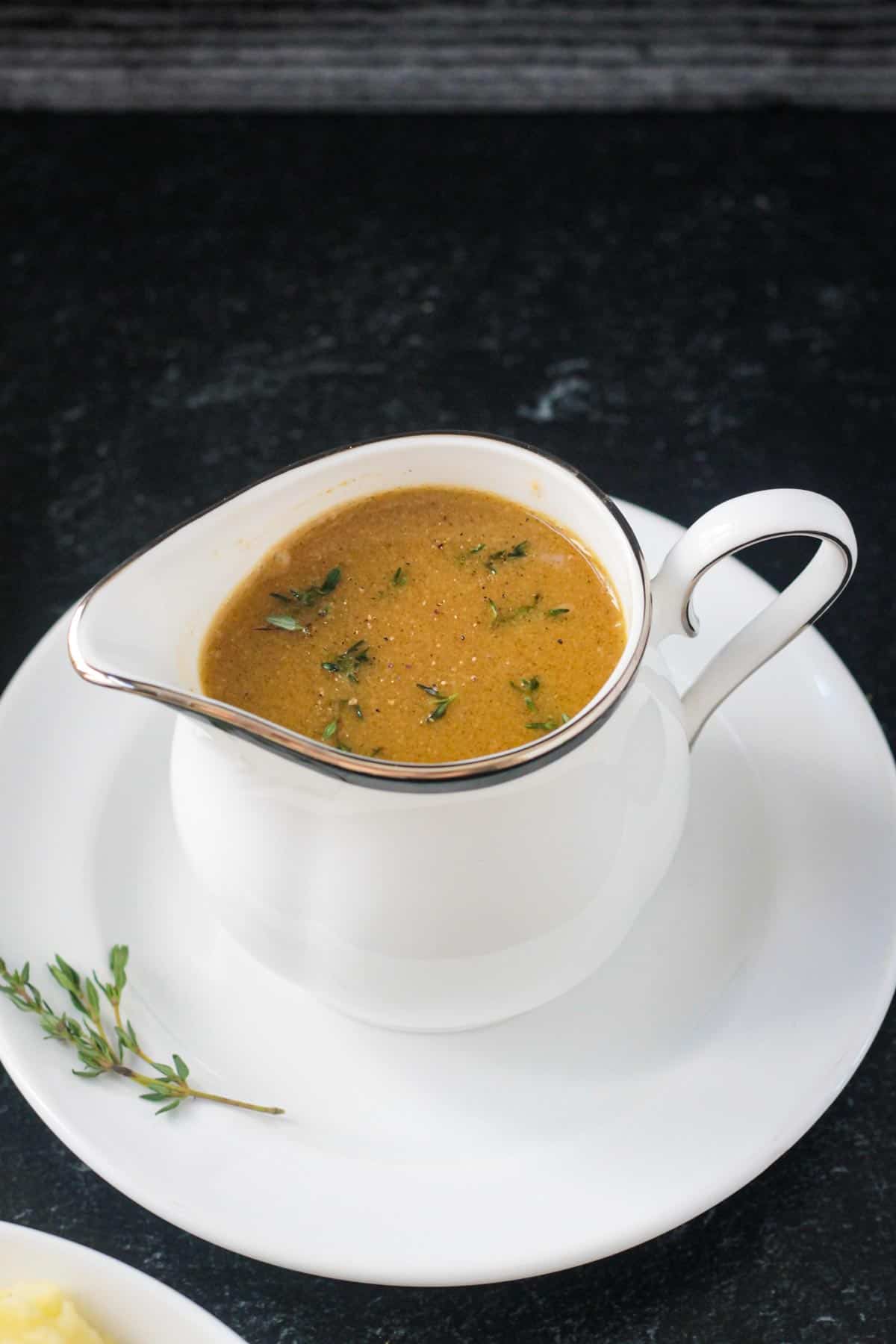 Small white pitcher of gravy garnished with fresh thyme leaves.
