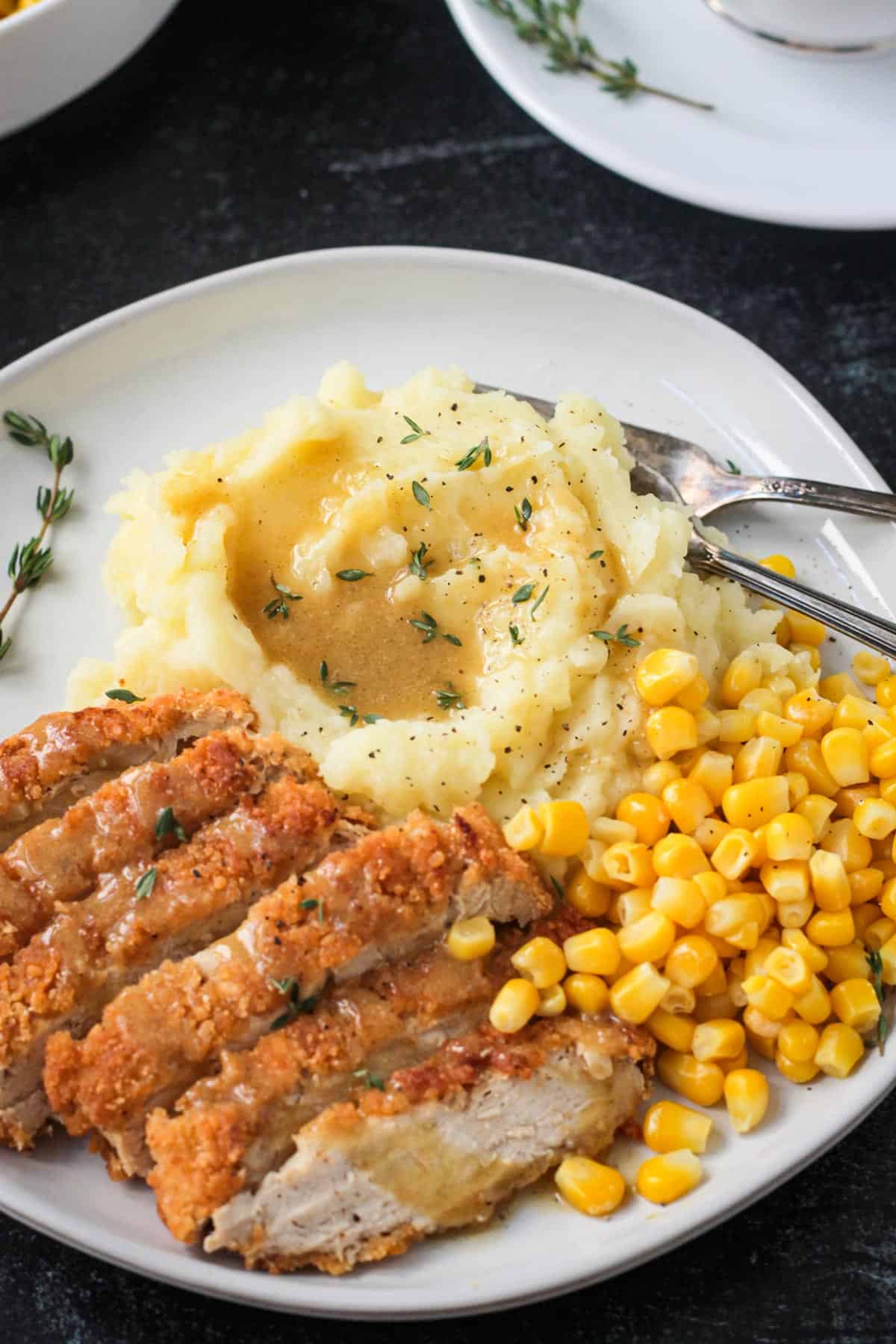 Close up of mashed potatoes topped with gravy on a plate with vegan chicken and corn.