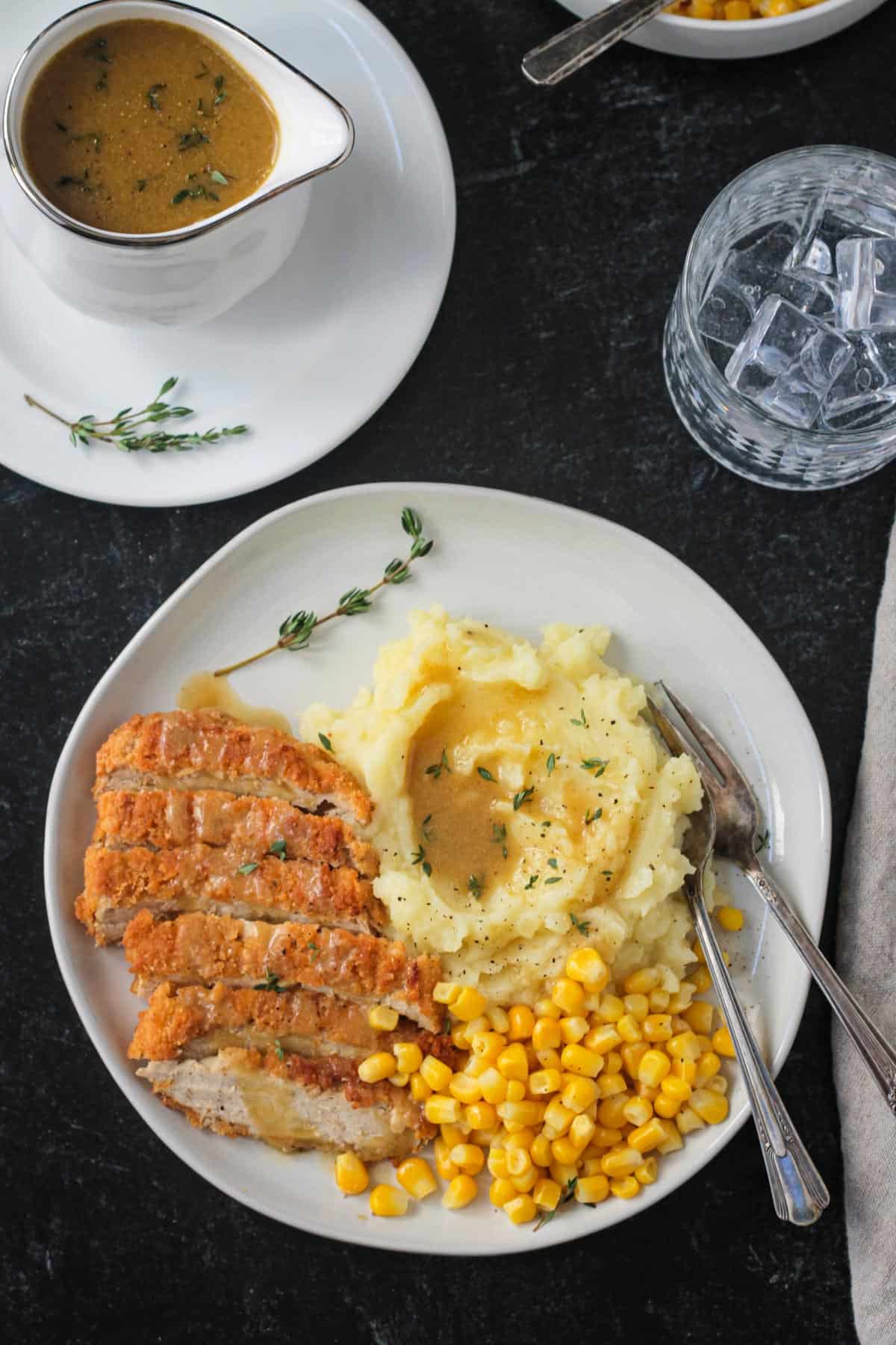Dinner plate with sliced vegan chicken, corn, and mashed potatoes with gravy.