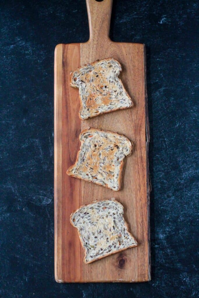 Three slices of toasted breads on a wooden serving board.