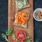 Cucumber hummus toast, carrot hummus toast, and tomato hummus toast on a serving board.