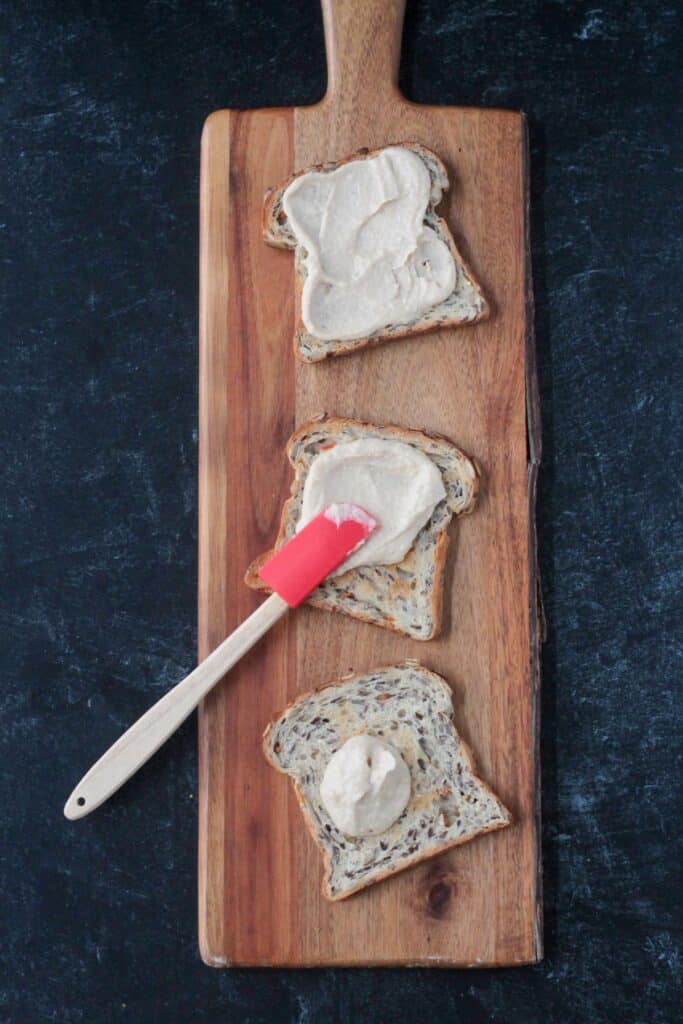 Spreading hummus on toast with a small red spatula.