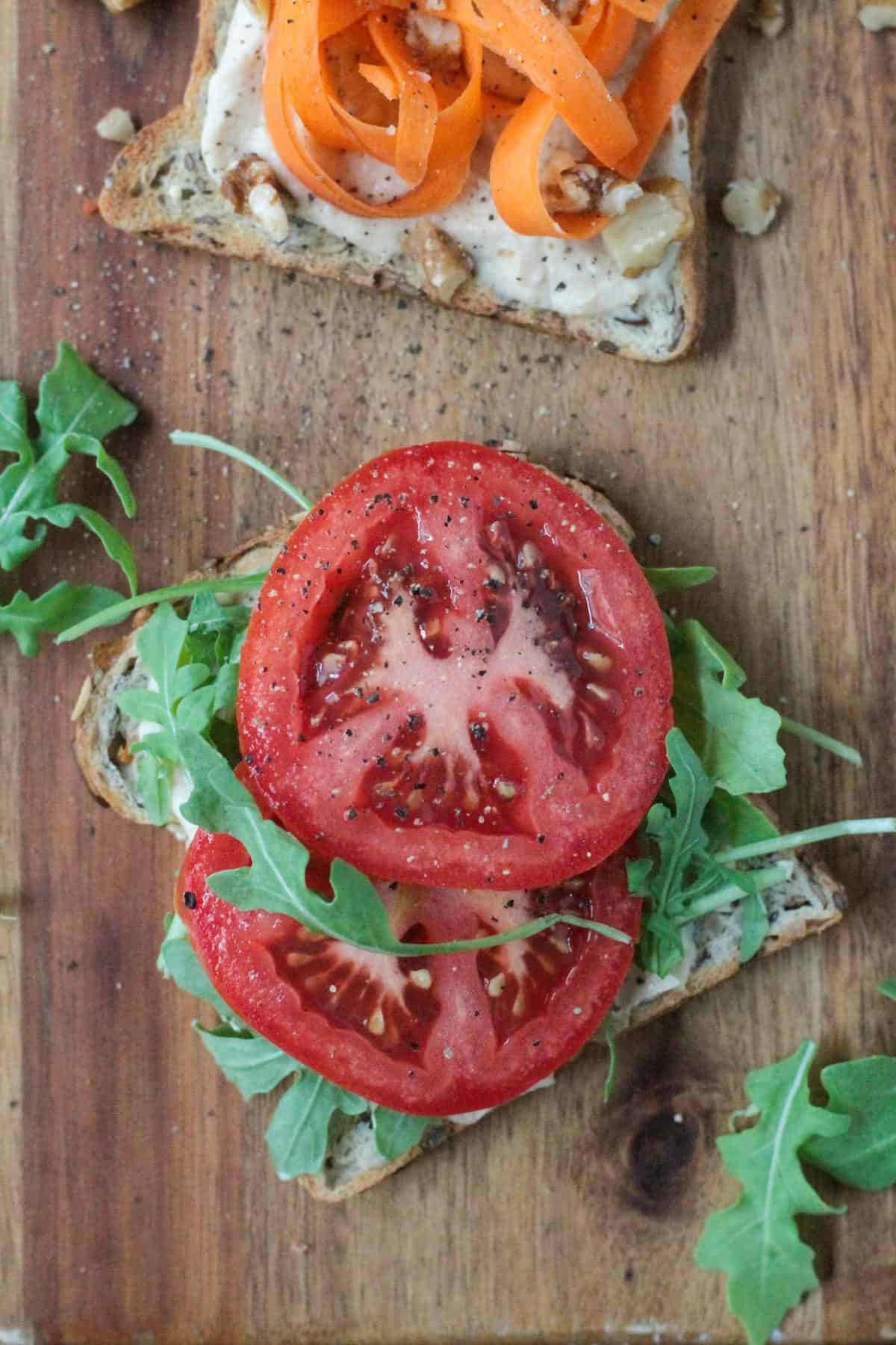 Hummus toast topped with two slices of tomato and arugula.