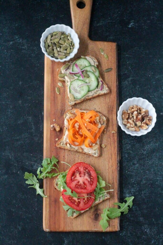 Cucumber hummus toast, carrot hummus toast, and tomato hummus toast on a serving board.