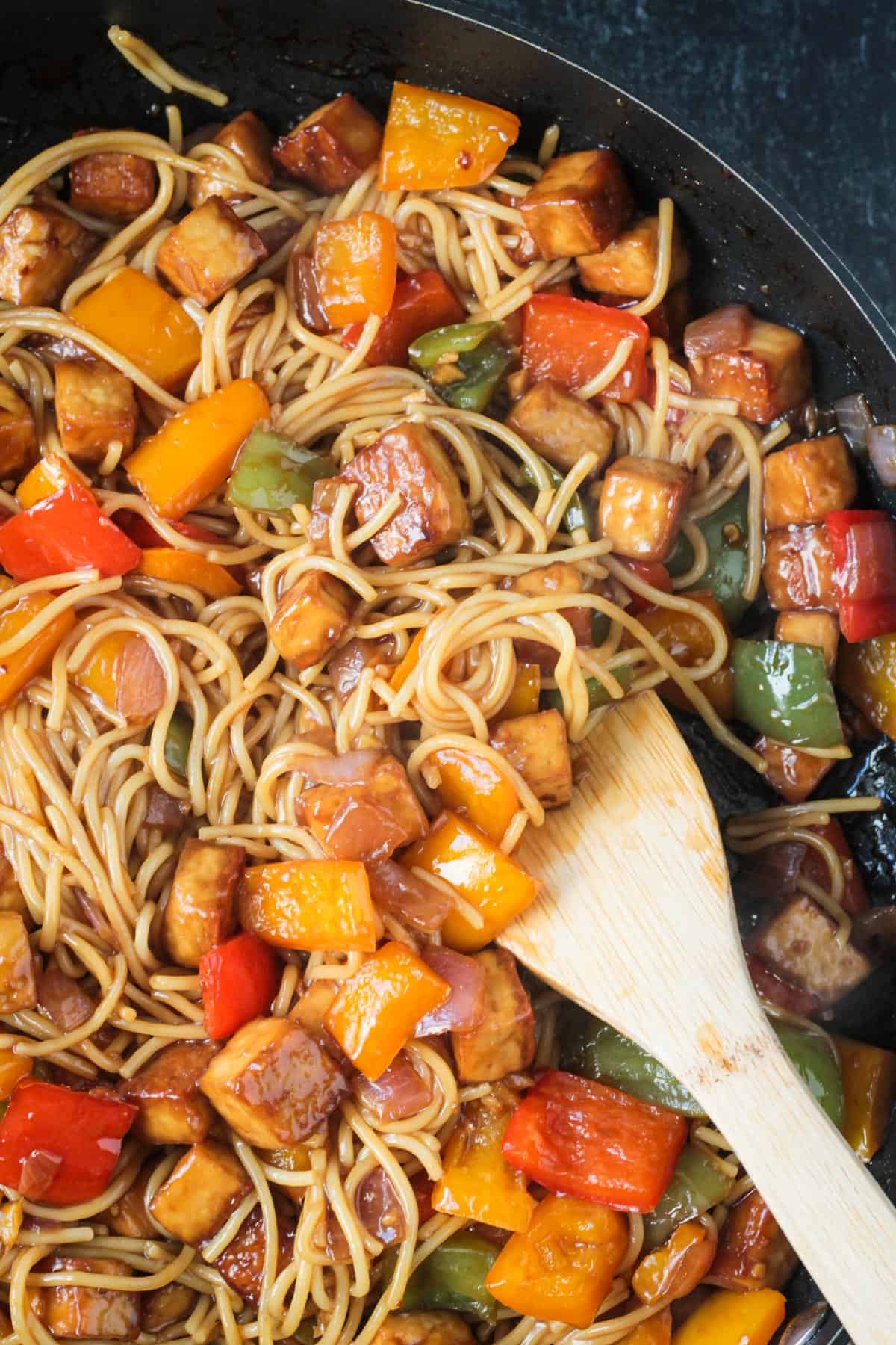 Close up of baked tofu, chopped peppers, and long noodles in a skillet.