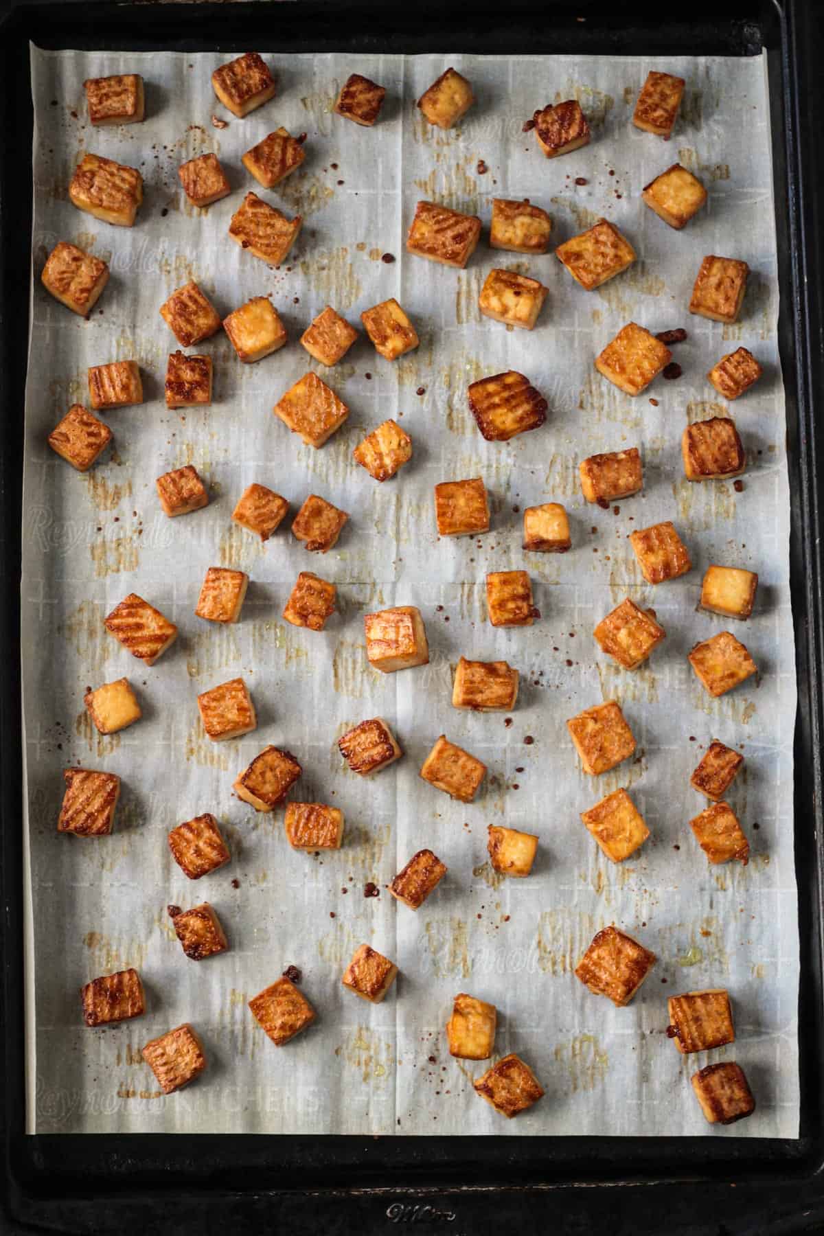 Baked tofu on a parchment lined baking sheet.