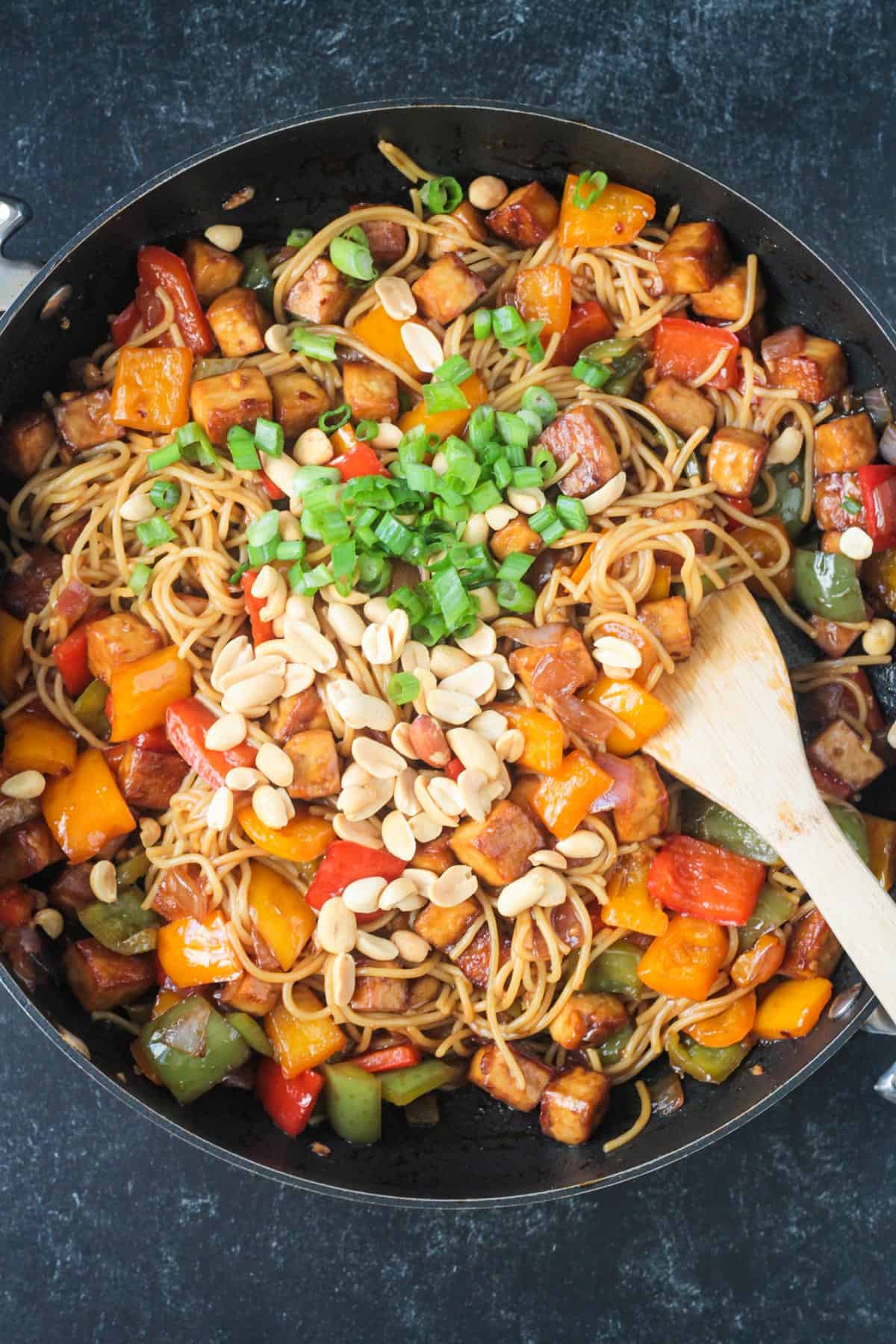 Sliced green onions and chopped peanuts sprinkled on top of veggies, noodles, and tofu in a skillet.