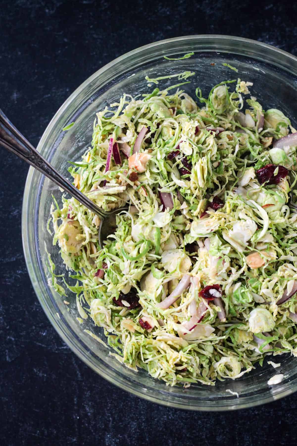 Close up of shaved brussels sprouts mixed with dried cranberries, sliced almonds, and red onions.