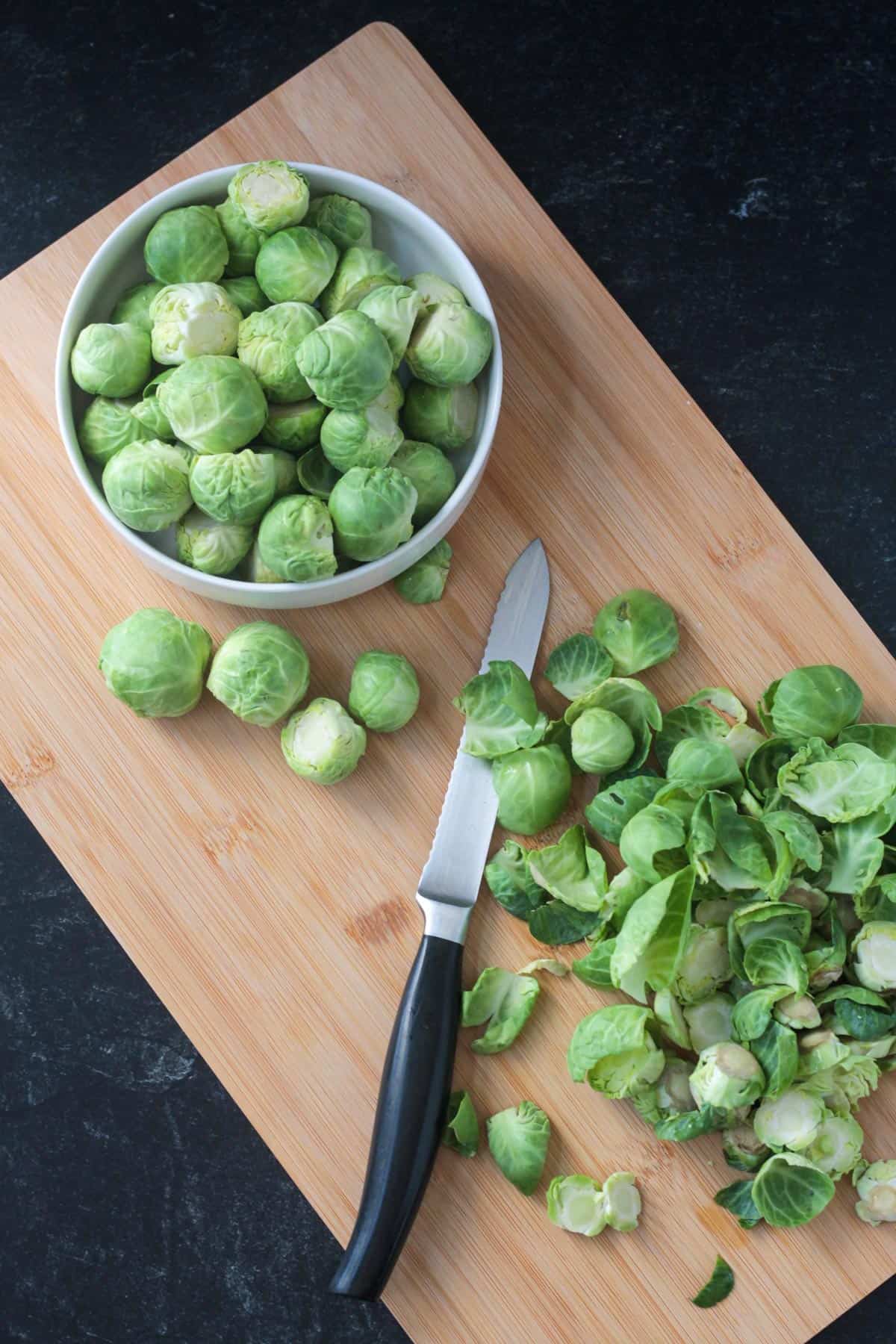 Brussels sprouts being trimmed on a cutting board with a serrated knife.