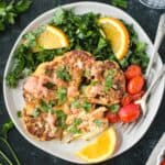 One roasted cauliflower steak garnished with spicy yogurt sauce and chopped parsley on a plate with kale salad and tomatoes.