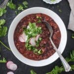 Vegan Black Bean Chili in a bowl with garnishes and a spoon.