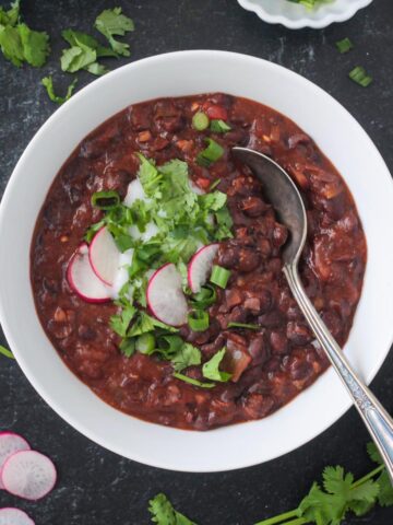 Vegan Black Bean Chili in a bowl with garnishes and a spoon.