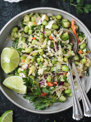 Cucumber edamame salad plated with two forks and two lime wedges.