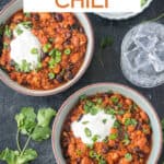 Two bowls of thick chili next to a glass of water.