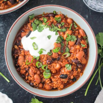 Vegan chorizo chili in a bowl with a dollop of sour cream and green onions.