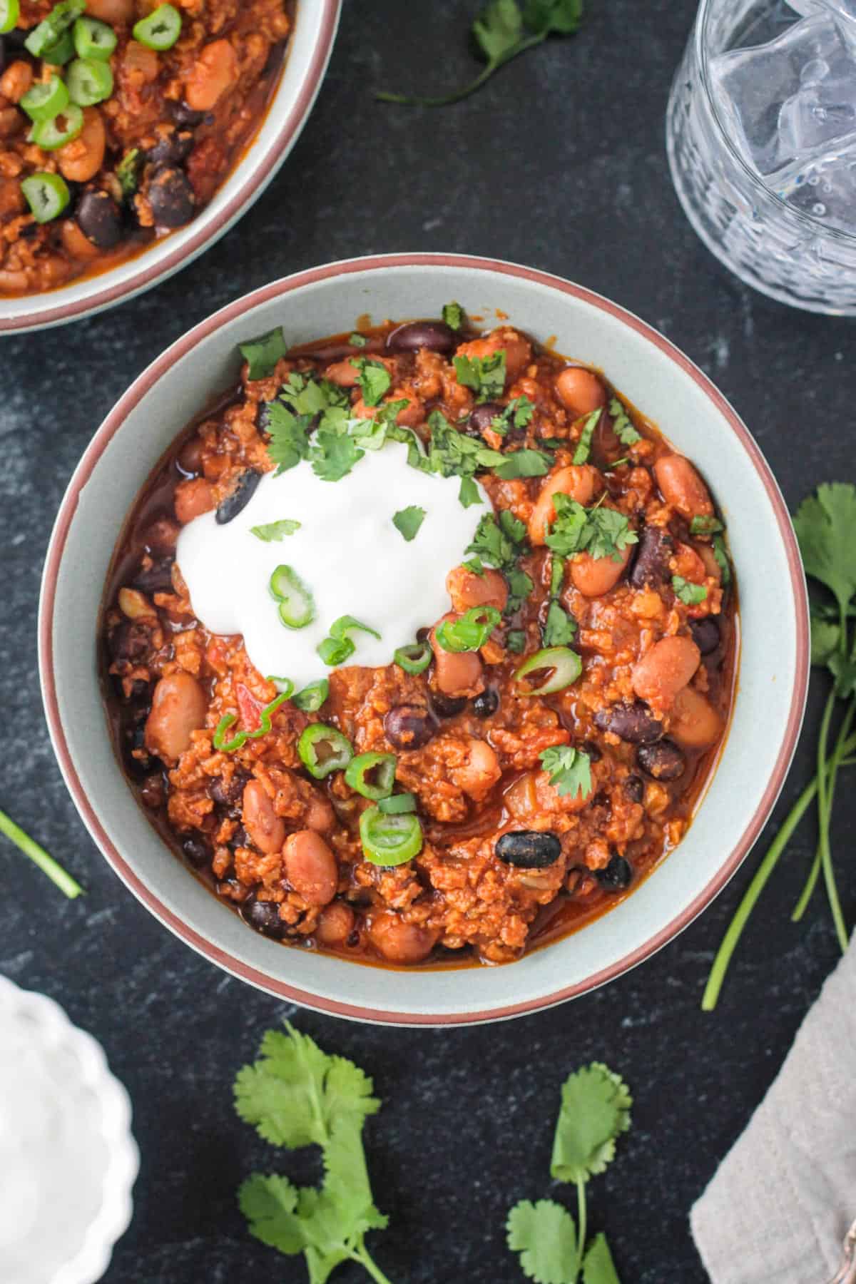 Vegan chorizo chili in a bowl with a dollop of sour cream and green onions.
