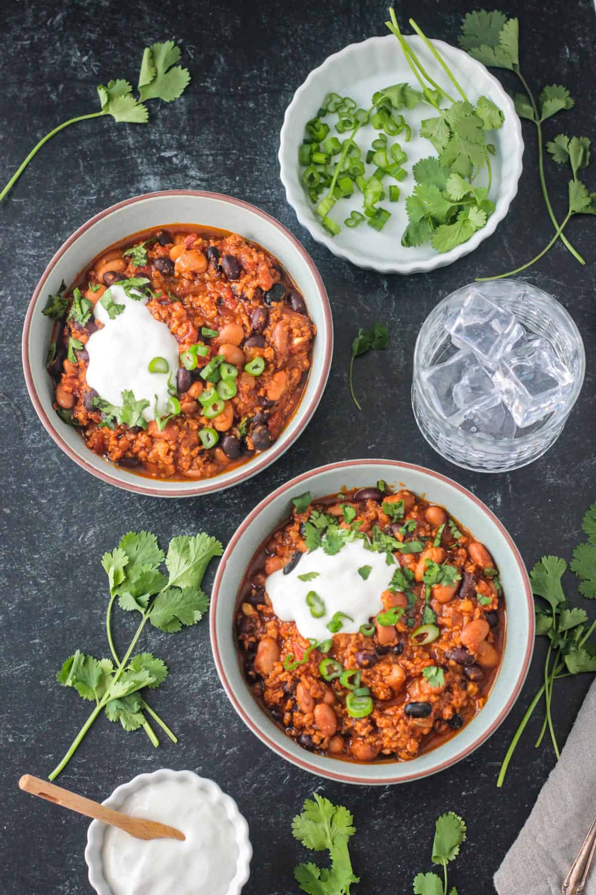 Two bowls of thick chili next to a glass of water.