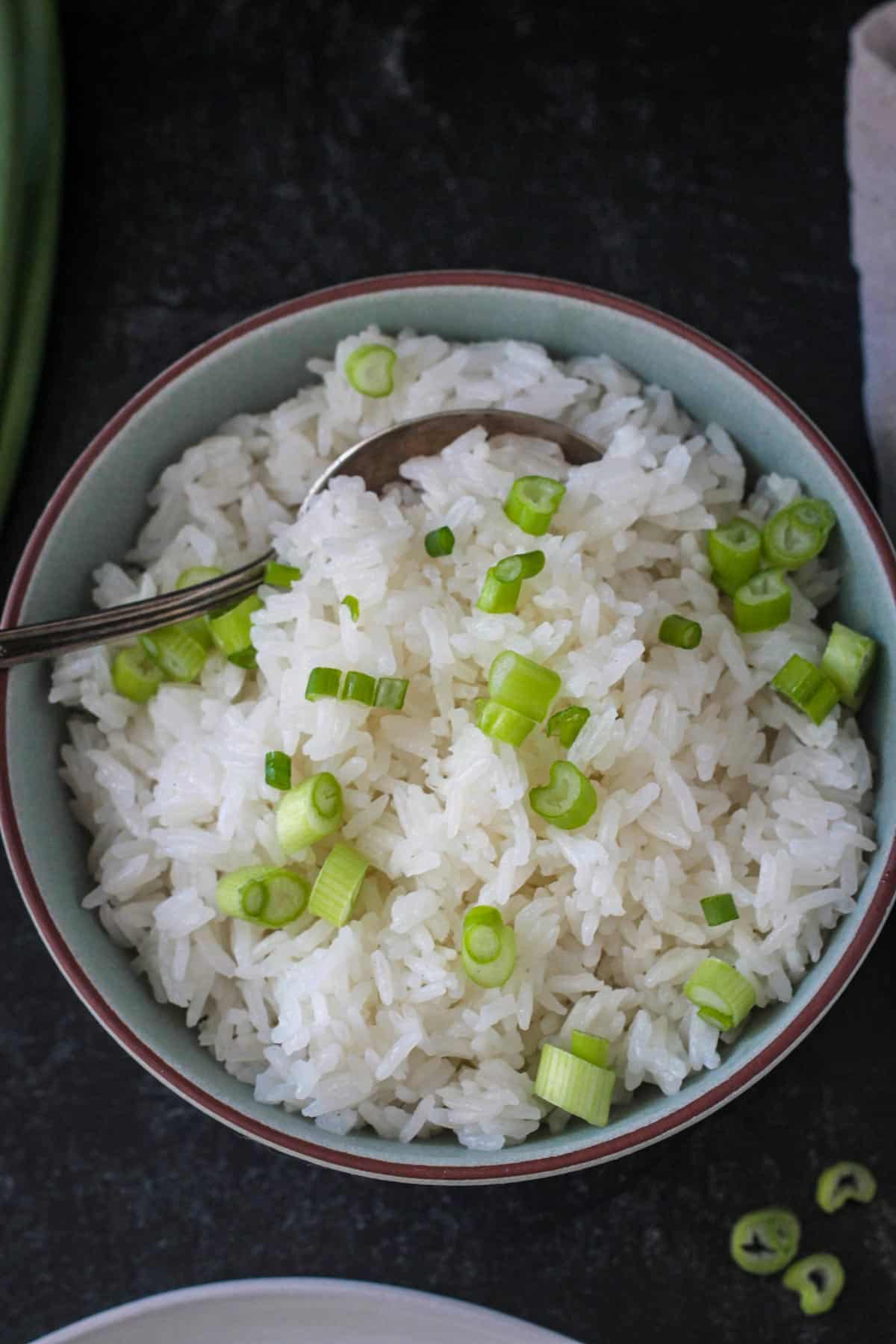 Fluffy coconut jasmine rice garnished with sliced green onions in a serving bowl.