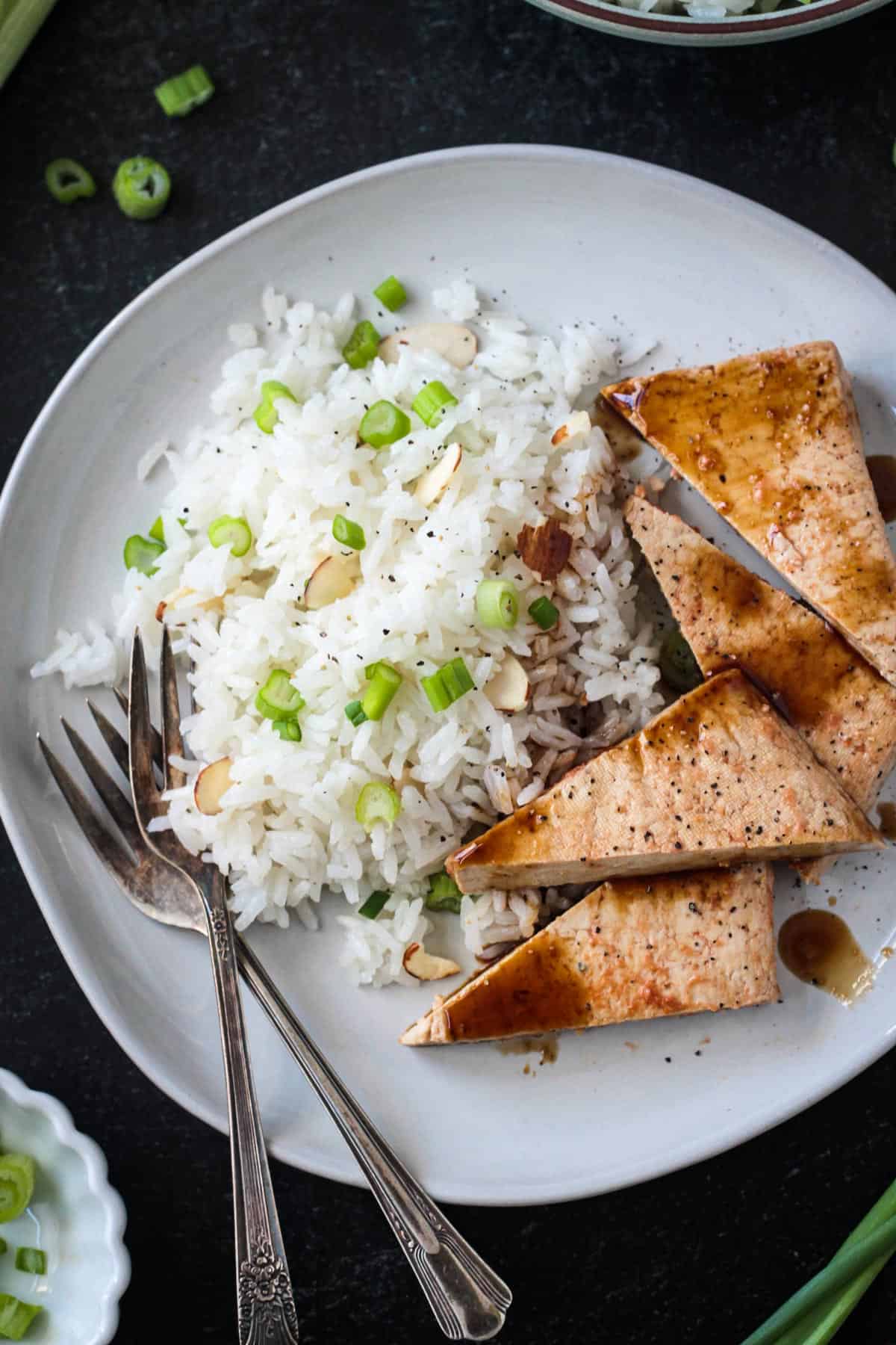 Coconut rice on a plate with triangles of baked tofu and two forks.