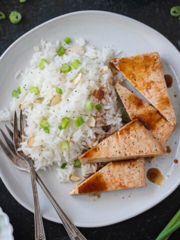 Coconut rice on a plate with triangles of baked tofu and two forks.