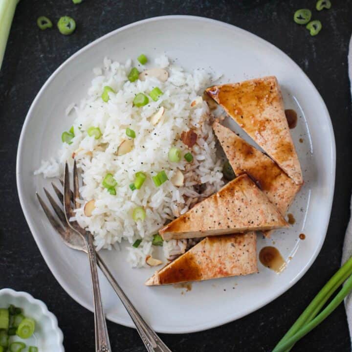 Coconut rice on a plate with triangles of baked tofu and two forks.