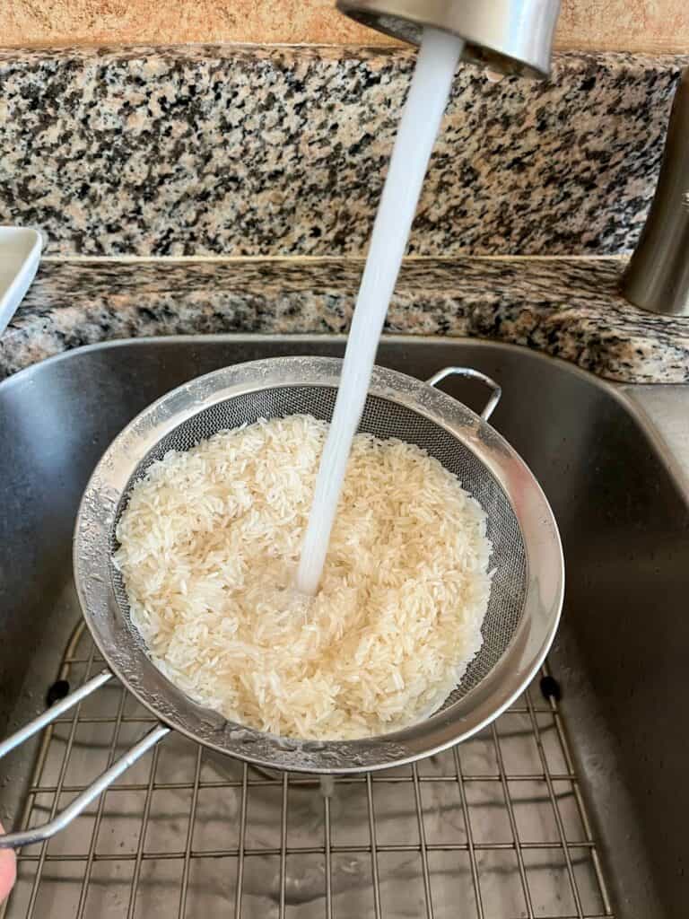 Rinsing rice in a fine mesh strainer with water.