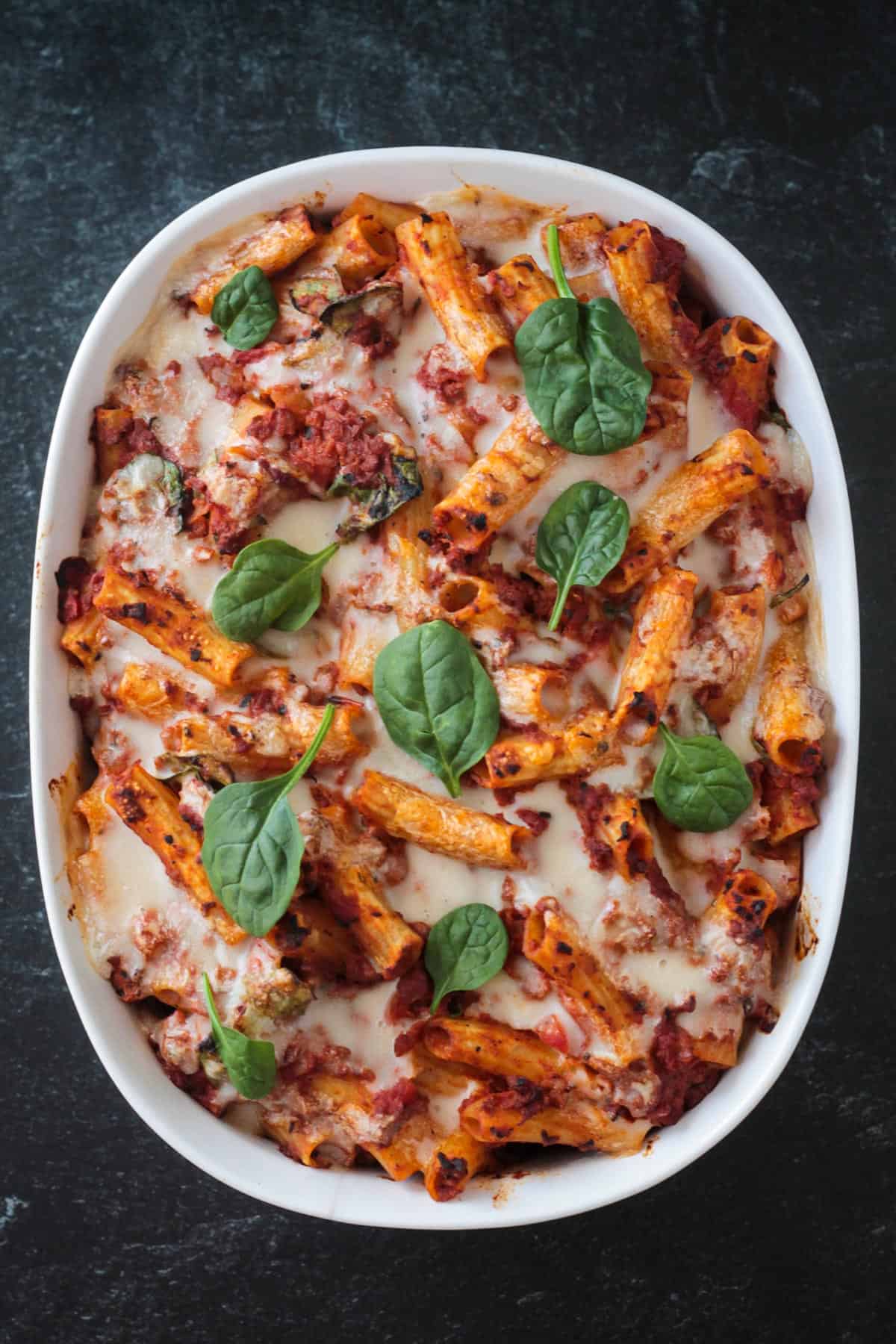 Vegan chorizo pasta bake in a casserole dish garnished with baby spinach leaves.
