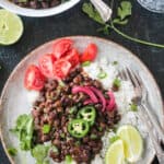 Serving of spicy seasoned black beans over coconut rice with a side of tomatoes.