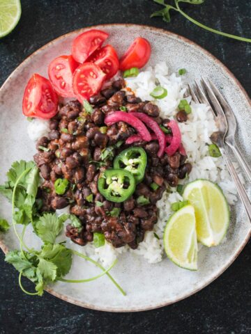 Serving of spicy seasoned black beans over coconut rice with a side of tomatoes.
