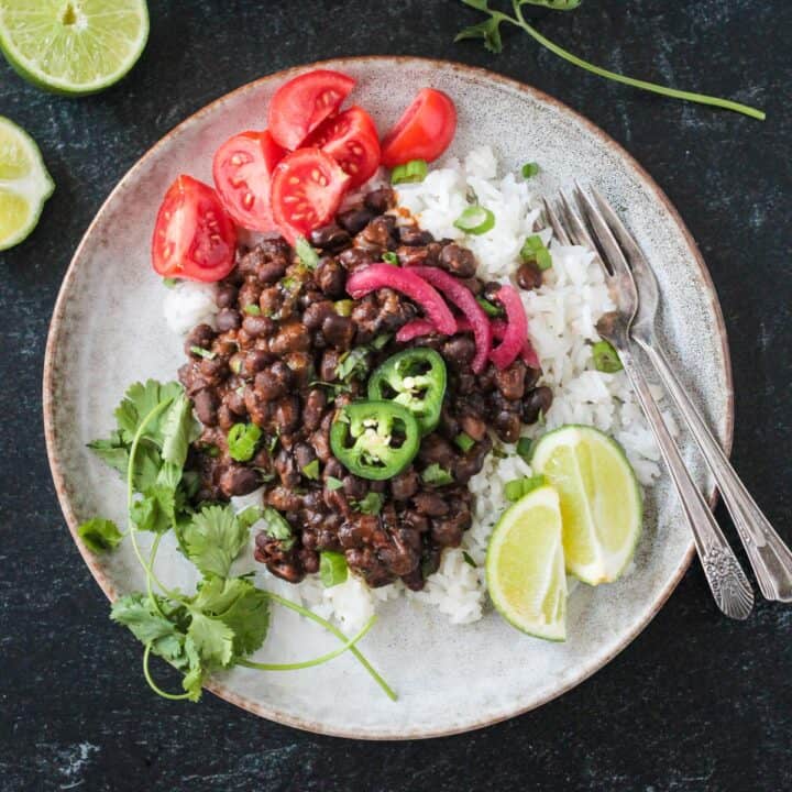 Serving of spicy seasoned black beans over coconut rice with a side of tomatoes.