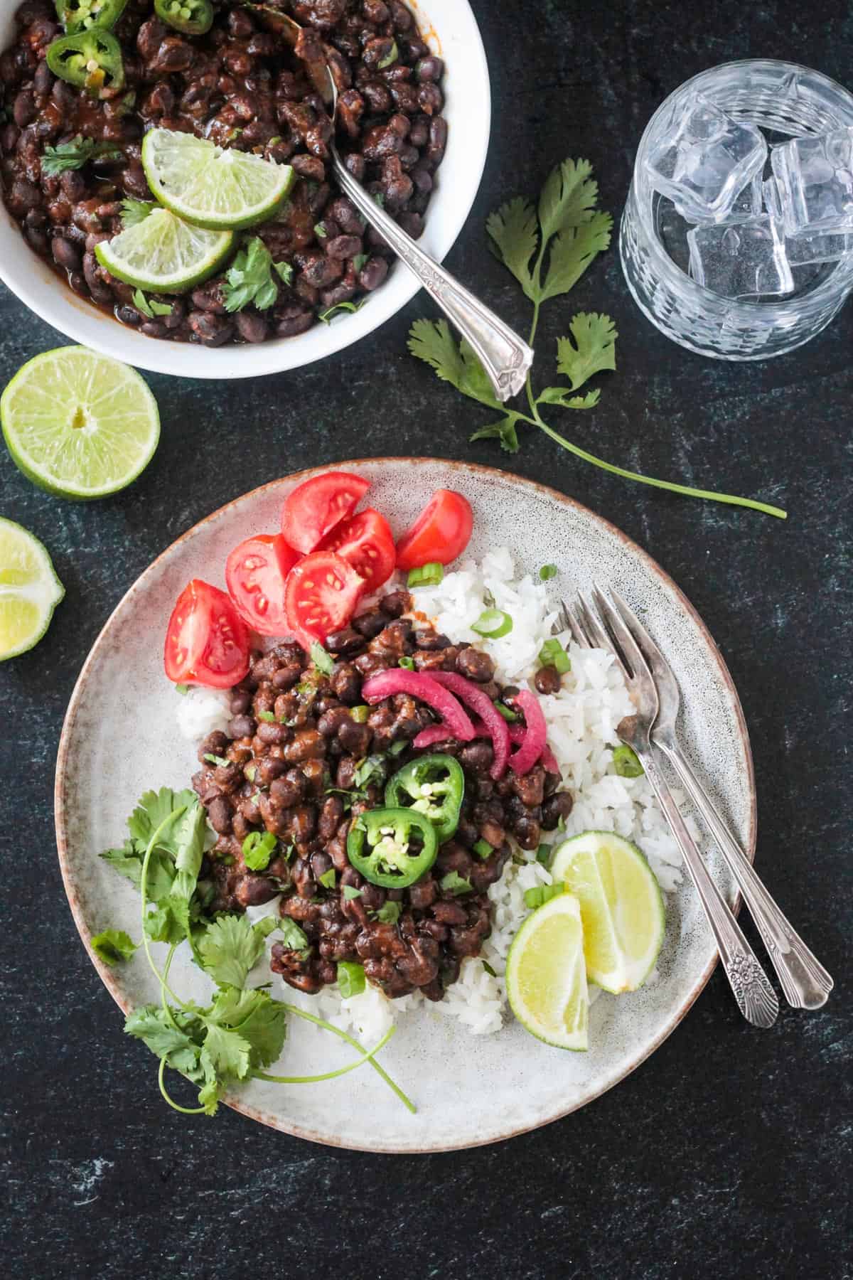 Serving of spicy seasoned black beans over coconut rice with a side of tomatoes.