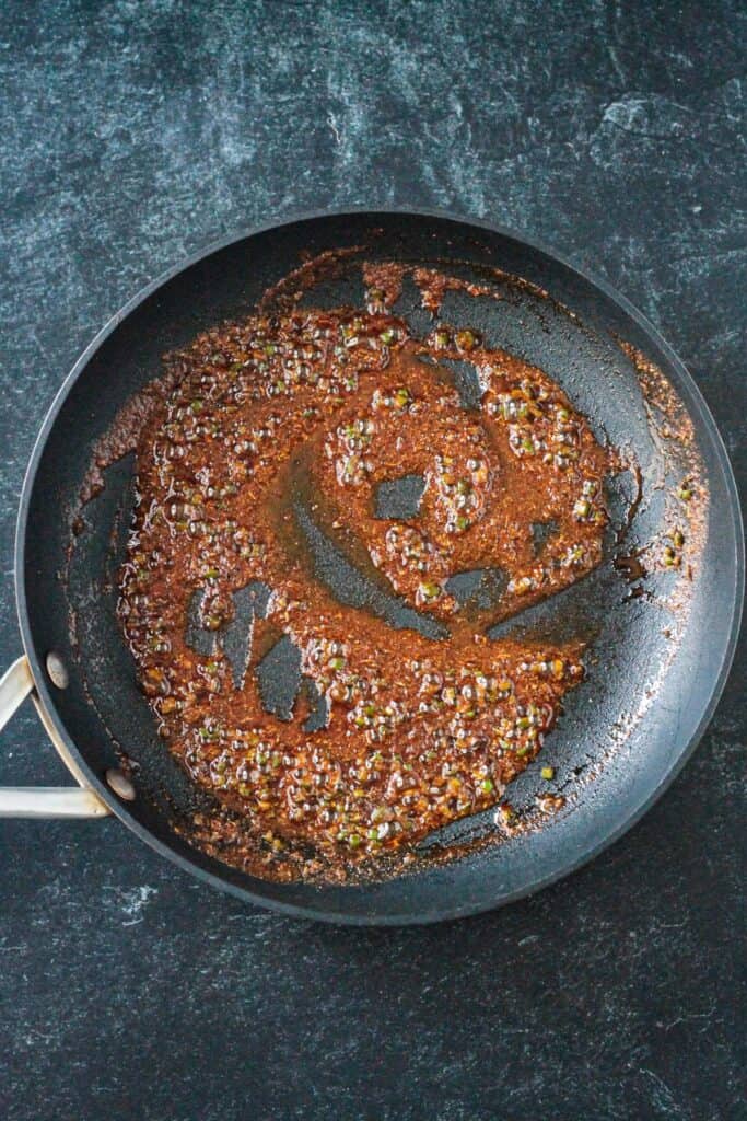 Spices simmering in oil in a skillet.