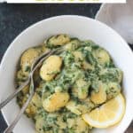 Close up of creamy spinach gnocchi on a fork in a bowl.