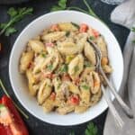 Creamy vegan beef pasta with peppers in a white bowl with two forks.