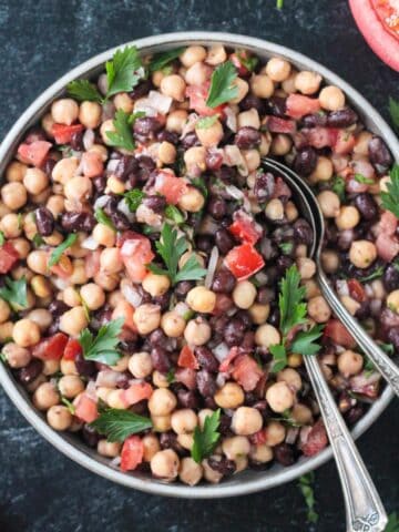 Middle Eastern balela salad in a mixing bowl with two spoons.