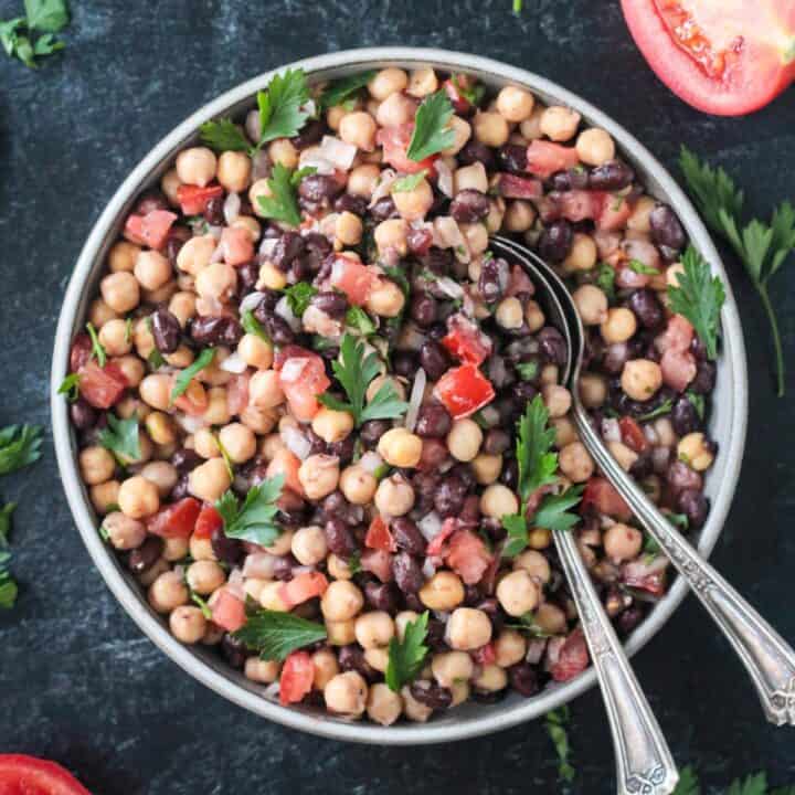 Middle Eastern balela salad in a mixing bowl with two spoons.